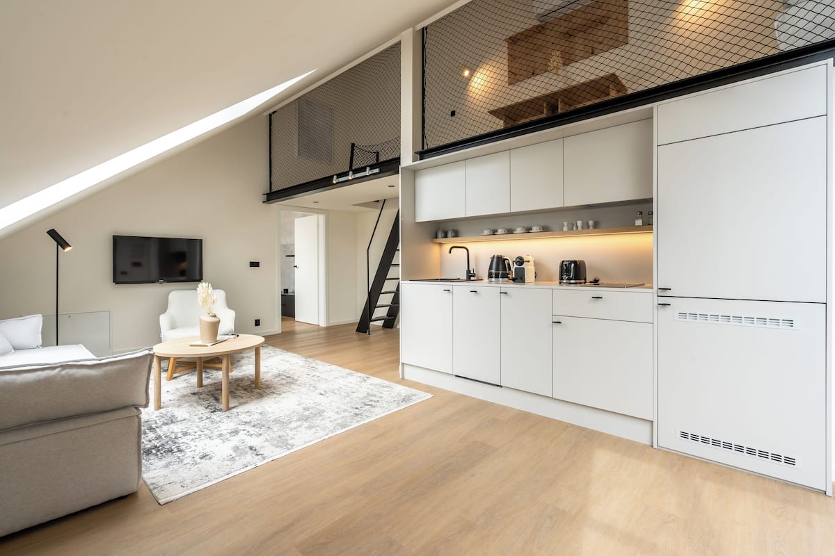 A modern loft apartment with a kitchen, living area, and a mezzanine with a balcony.