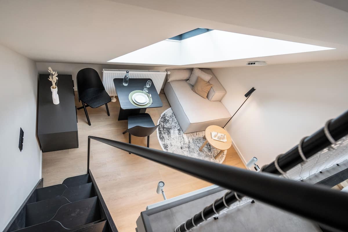 A modern, compact living space with a dining area, sofa, and staircase.