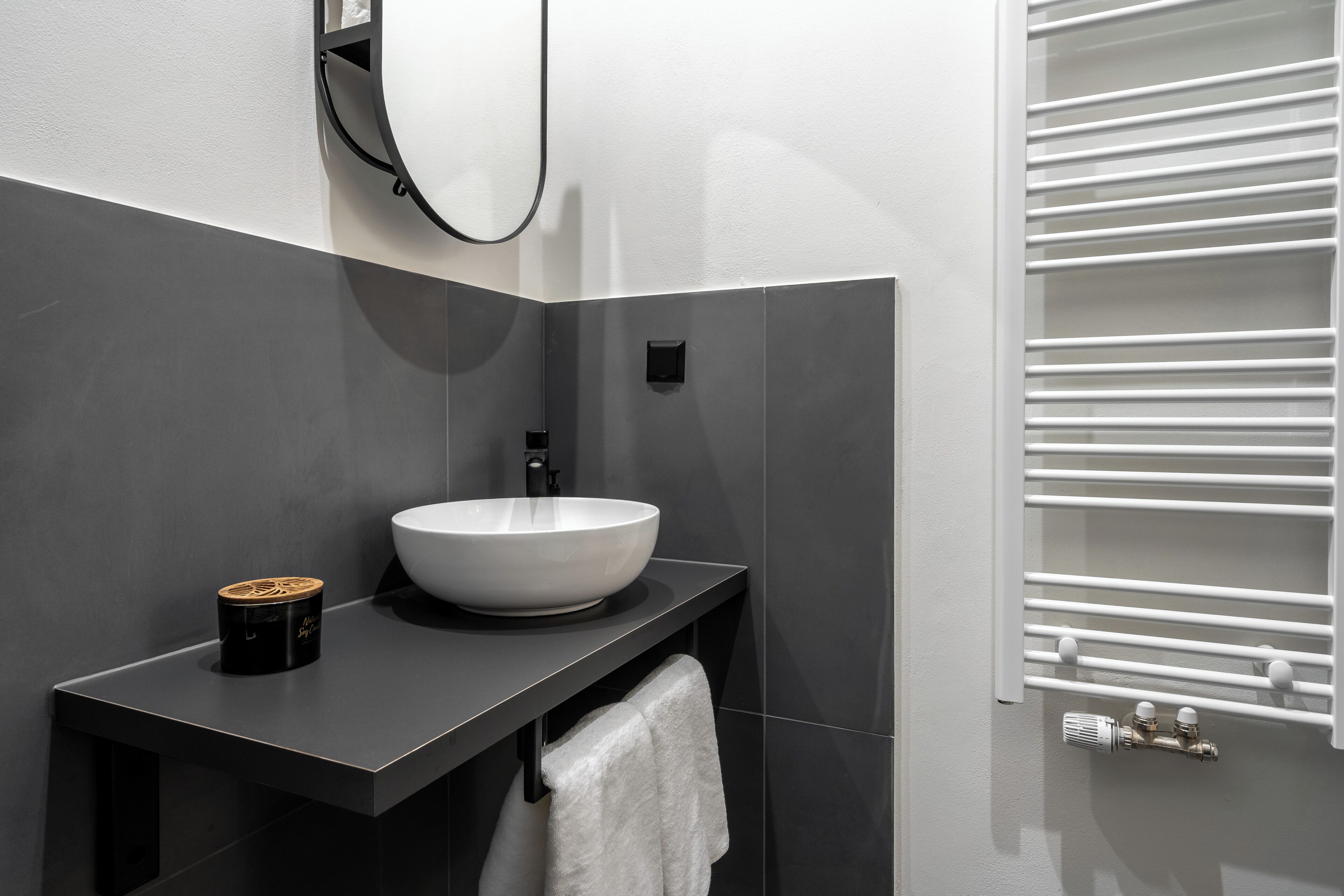Un baño moderno con un lavabo blanco tipo recipiente, una encimera negra, un perchero y una toalla colgada en la pared.