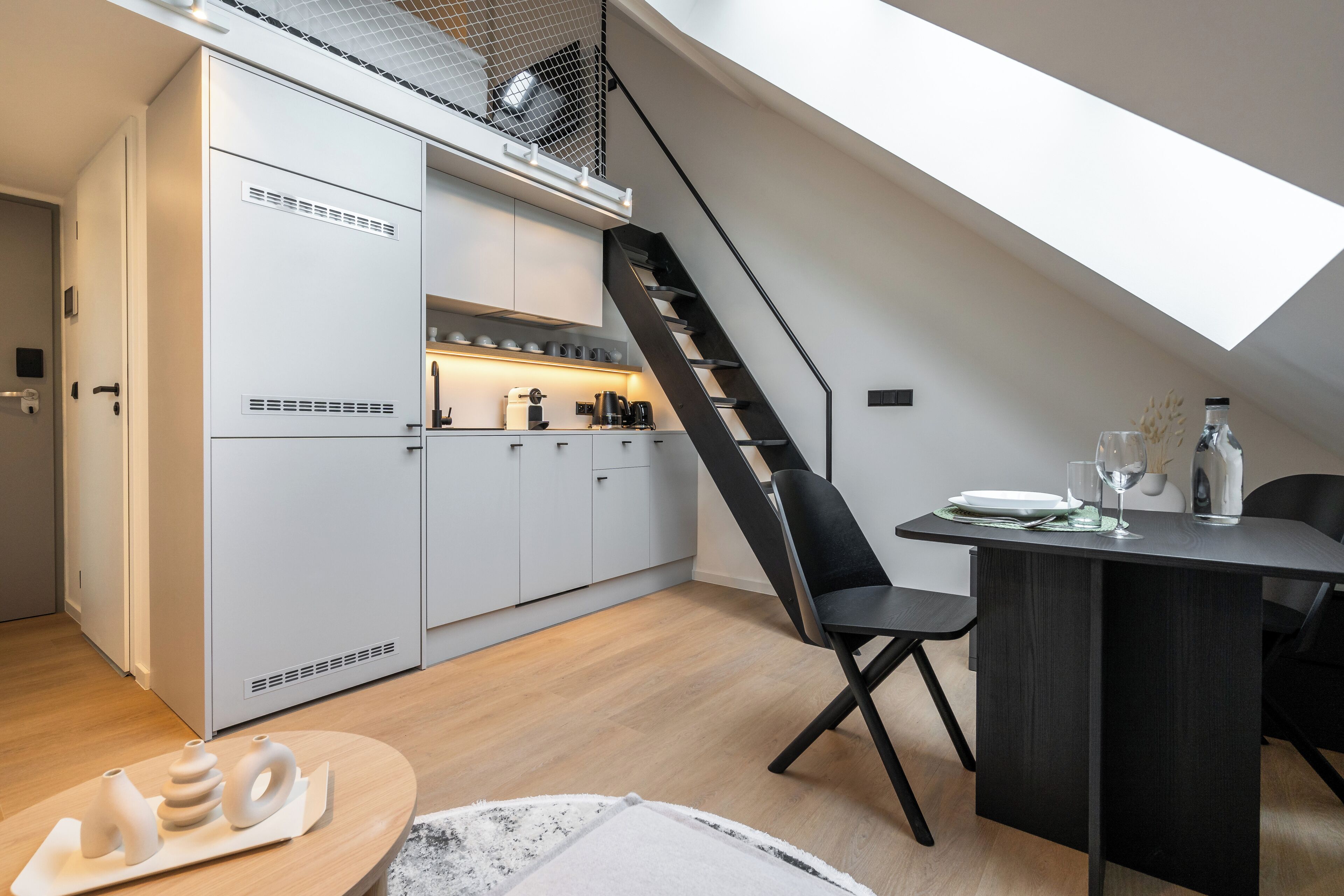 Eine moderne Küche mit weißen Schränken, einer schwarzen Treppe und einem Essbereich mit Tisch und Stühlen.