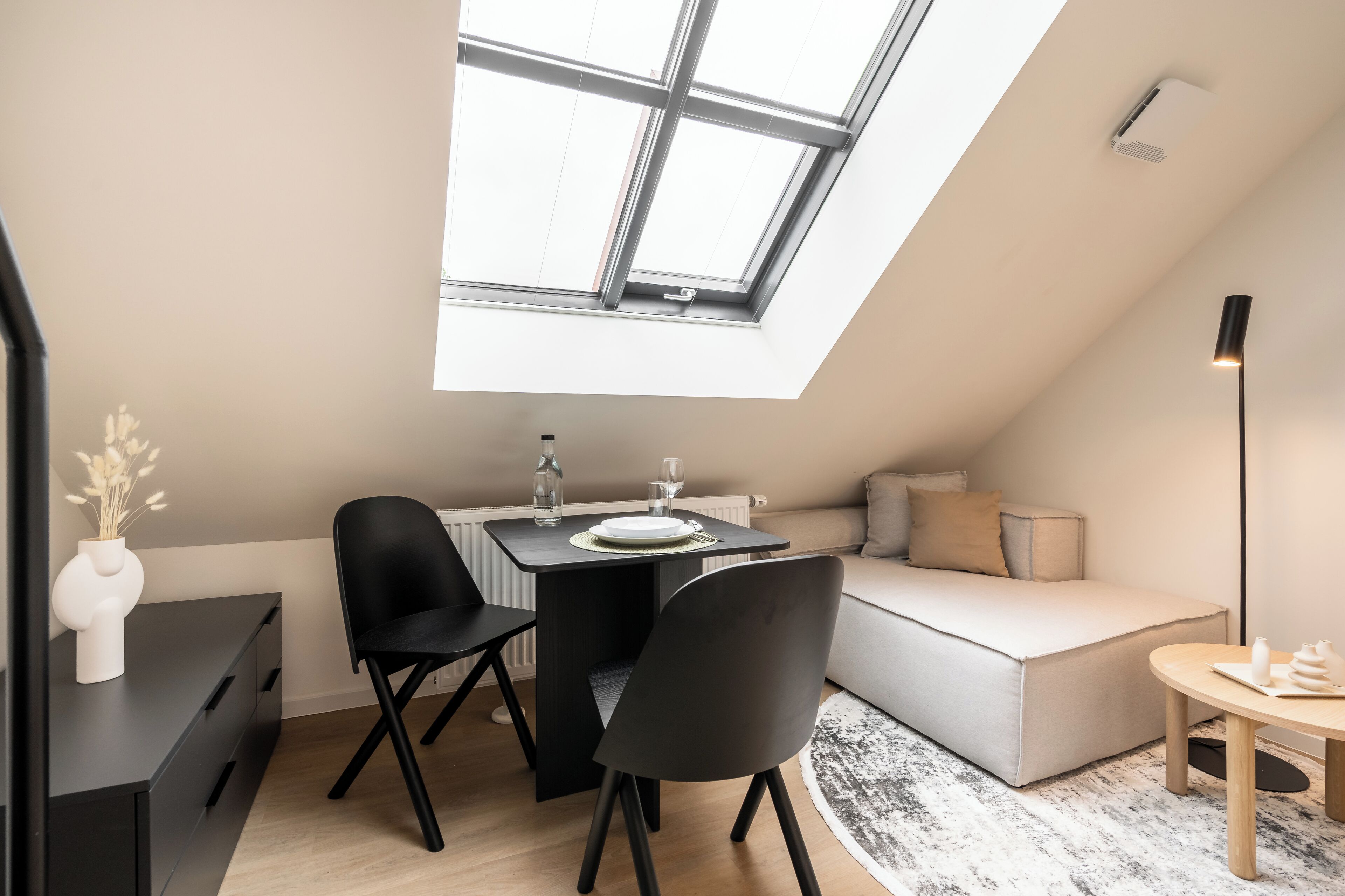A modern loft apartment with a skylight, a dining area, a sofa, and a small round table.