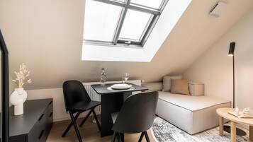 A modern loft apartment with a skylight, a dining area, a sofa, and a small round table.