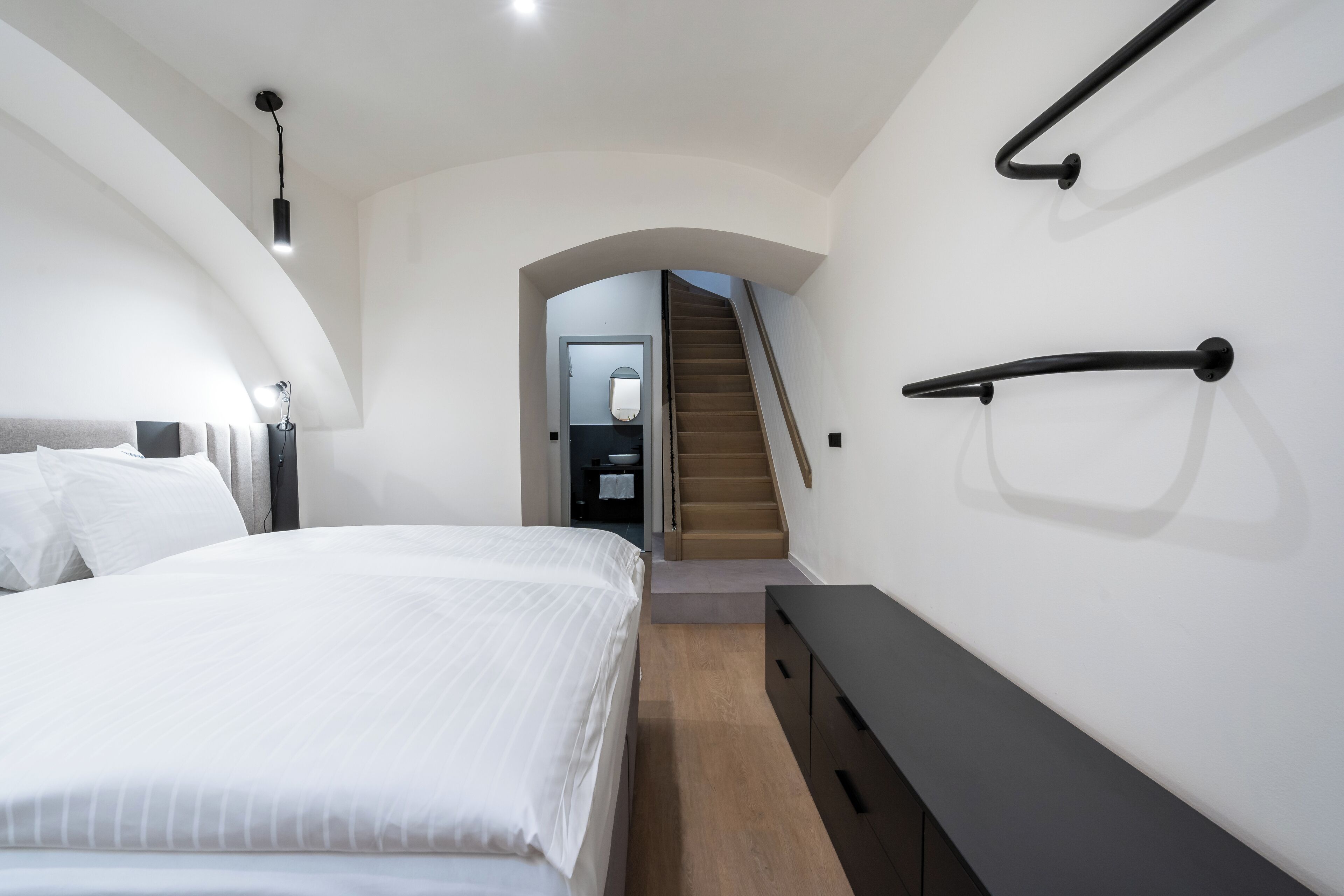 Un dormitorio moderno con una cama grande, un aparador y una escalera que lleva a un nivel superior.