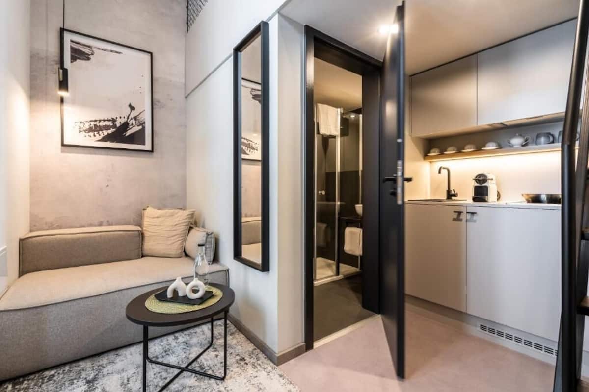 A modern apartment with a sofa, a small table, a kitchen with cabinets and a sink, and a framed picture on the wall.