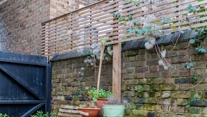 A brick wall with a wooden bench and table, potted plants, and a black gate. - Trendy 2BD House 5 Mins From Willesden Junction! (London)