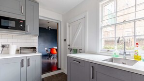 A kitchen with grey cabinets, a microwave, a toaster, and a window with a view of the outside. - Trendy 2BD House 5 Mins From Willesden Junction! (London)