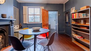 A dining area with a round table, colorful chairs, a bookshelf, and a window with a view. - Trendy 2BD House 5 Mins From Willesden Junction! (London)