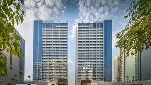 A modern high-rise building with a grid of windows and balconies, surrounded by other buildings and greenery. - Vogue | Sterling Downtown near Dubai Mall | Burj Khalifa (Dubai)