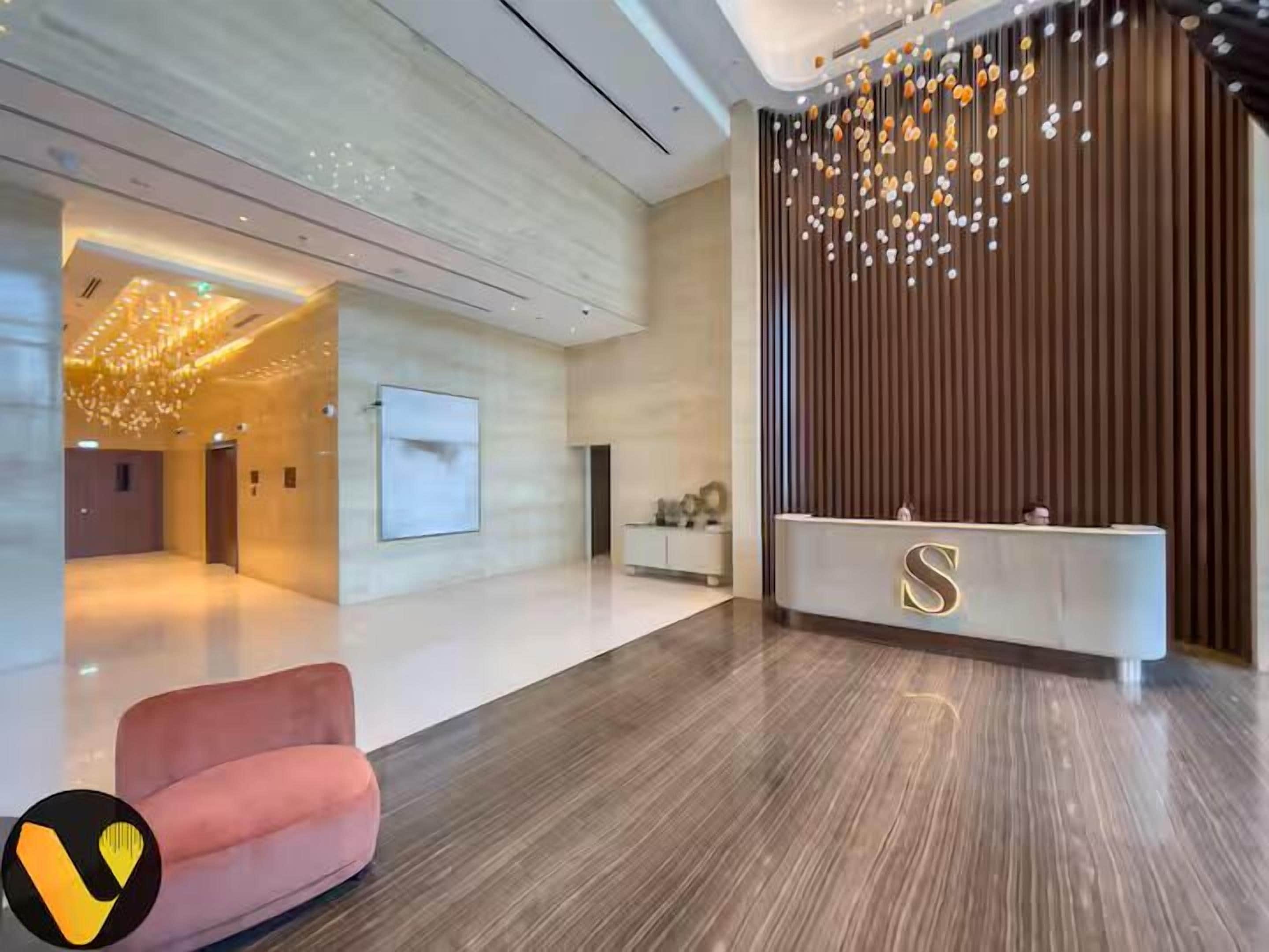 Een moderne lobby met een receptiebalie, een roze bank en een decoratieve lamp.