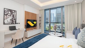 A modern hotel room with a large bed, a desk with a laptop, a TV mounted on a wooden panel, and a balcony with a city view. - Vogue | Sterling Downtown near Dubai Mall | Burj Khalifa (Dubai)