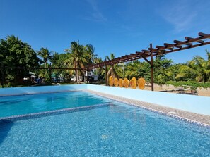 A clear blue pool with a tiled edge, surrounded by palm trees and a pergola structure. - Yemaya de Laiya powered by Cocotel (San Juan)