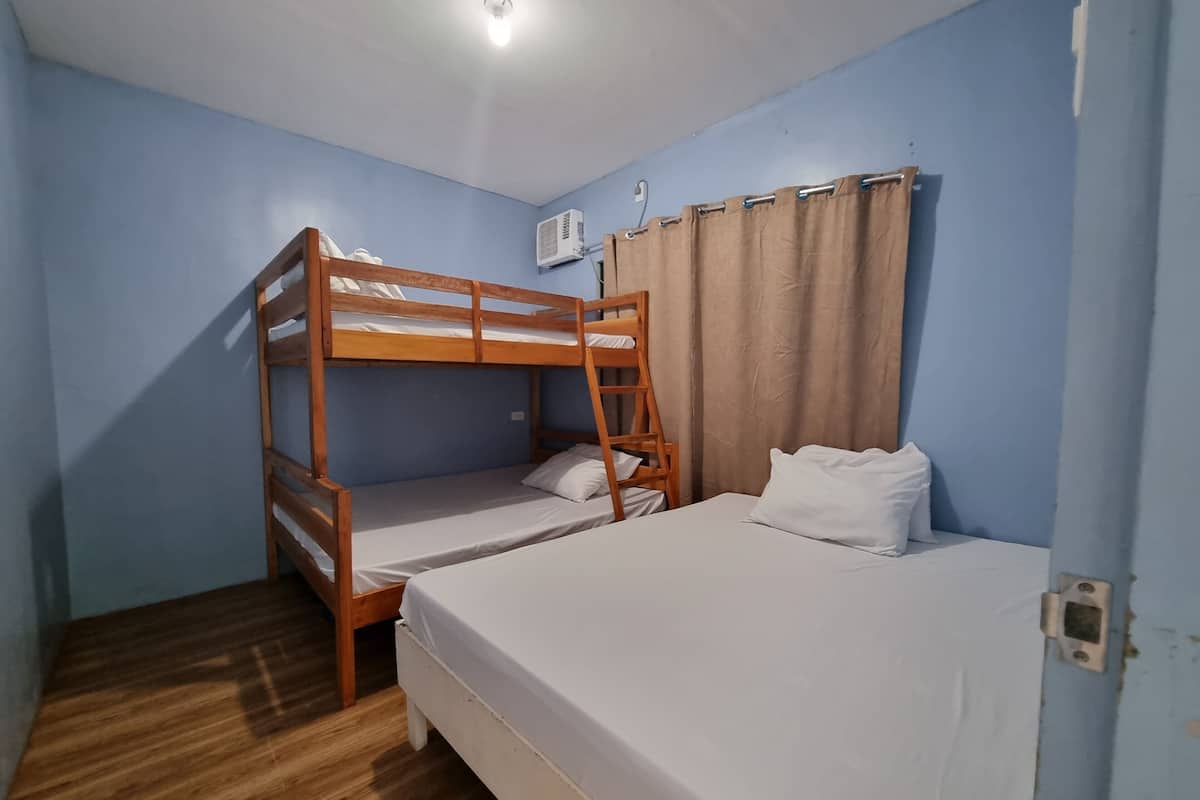 Una habitación con literas, una cama individual, una escalera de madera, una cortina y un equipo de aire acondicionado.