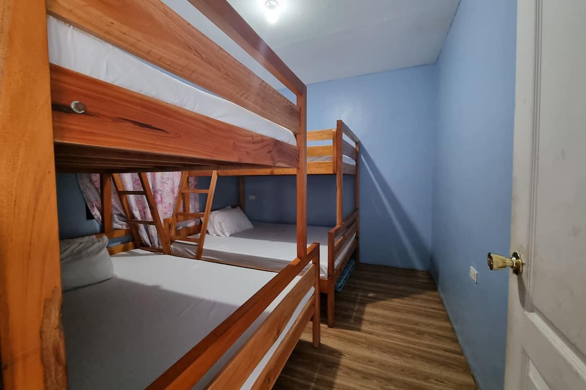 Una habitación con tres literas, suelo de madera y una puerta con picaporte de latón.