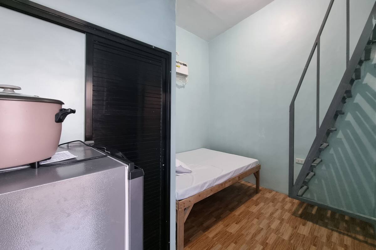 Una habitación compacta con kitchenette, una cama individual y una escalera.