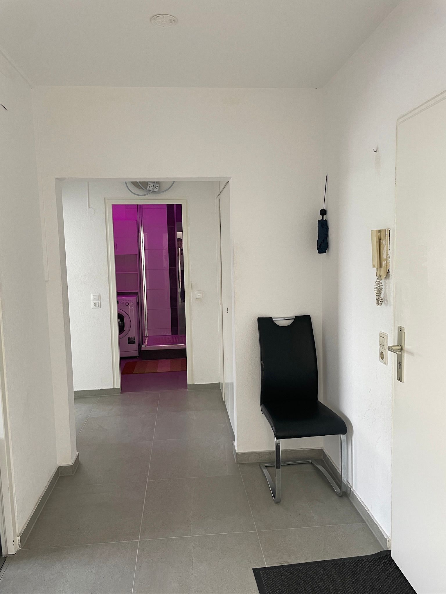 A hallway with a chair, a door with a phone, and a wall socket.