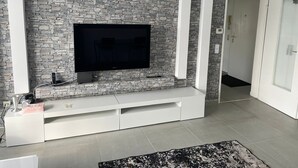 Un salon moderne avec un mur en pierre, un téléviseur à écran plat, un meuble de rangement intégré blanc et un tapis noir et blanc.
