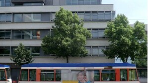Un autobus arborant une grande publicité sur son flanc est garé devant un immeuble moderne à plusieurs étages, doté de grandes fenêtres.