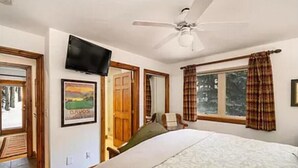 Una camera da letto con un letto, una ventola a soffitto, una TV, una finestra con tende e una porta.