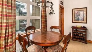 Zona pranzo con tavolo rotondo in legno, quattro sedie, un lampadario, un portavino e un quadro appeso al muro.