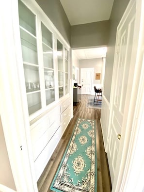 A hallway with a patterned rug, a glass-fronted cabinet, and a door leading to another room.