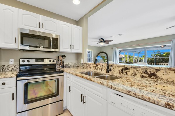 A modern kitchen with white cabinets, a stainless steel oven, a microwave, and a granite countertop.