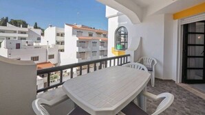 A balcony with a table and chairs, a view of neighboring buildings, and a door with a window. - Spacious central beach home steps from the sea (Carvoeiro)