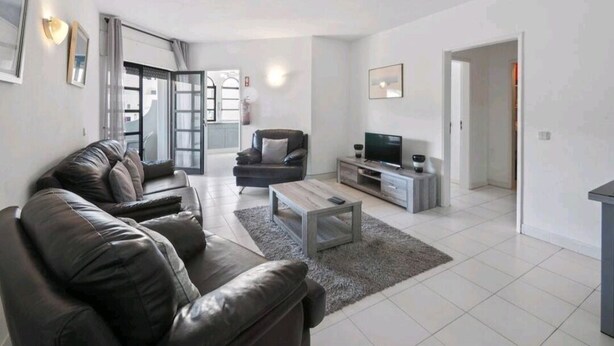 A modern living room with a sofa, coffee table, TV, and a dining area. - Spacious central beach home steps from the sea (Carvoeiro)