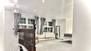 A spacious room with a high ceiling, a staircase with a wooden railing, and a large window with curtains. - Spacious One Bedroom Cottage
 (Trowbridge)