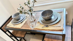 A dining table with two sets of plates, bowls, and cutlery, accompanied by a vase with branches. - Spacious One Bedroom Cottage
 (Trowbridge)