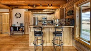 A rustic kitchen with wooden cabinets, a central island with stools, and a large window offering a view. - ********River Cabin Minutes To Town***** (Hamilton)