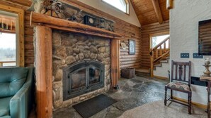 A log cabin interior with a stone fireplace, a green leather sofa, and a wooden staircase. - ********River Cabin Minutes To Town***** (Hamilton)