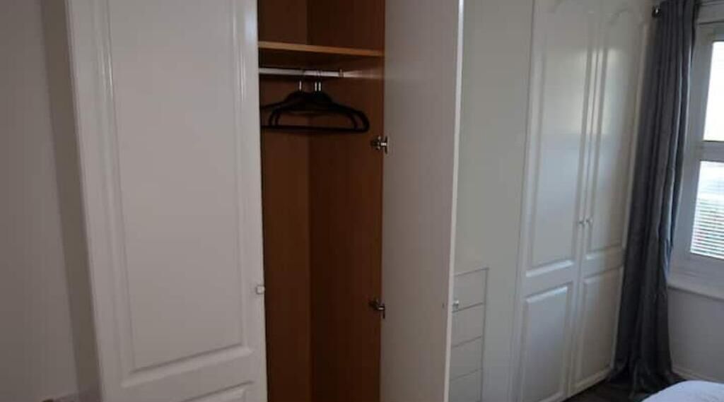 A room with a wardrobe, a hanging rack, and a window with curtains.