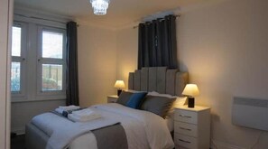 A bedroom with a bed, bedside tables, lamps, a window with curtains, and a wall-mounted air conditioner.