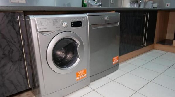A compact, modern kitchen with a built-in washer and dryer, a marble backsplash, and a tiled floor.