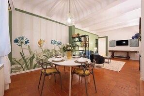 Un coin repas avec une table ronde, des chaises, un luminaire suspendu, une bibliothèque et un téléviseur fixé au mur.