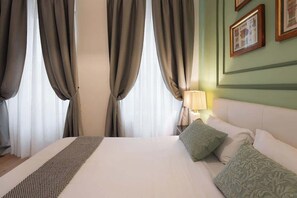 Ein Hotelzimmer mit einem großen Bett, Vorhängen, einem Nachttisch mit Lampe sowie gerahmten Bildern an der Wand.