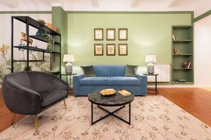 Un salon avec un canapé bleu, un fauteuil noir, une table basse ronde et un mur d’accent vert.