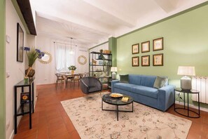Un salon avec un canapé bleu, une table basse, une bibliothèque et un coin repas comprenant des chaises et une table.