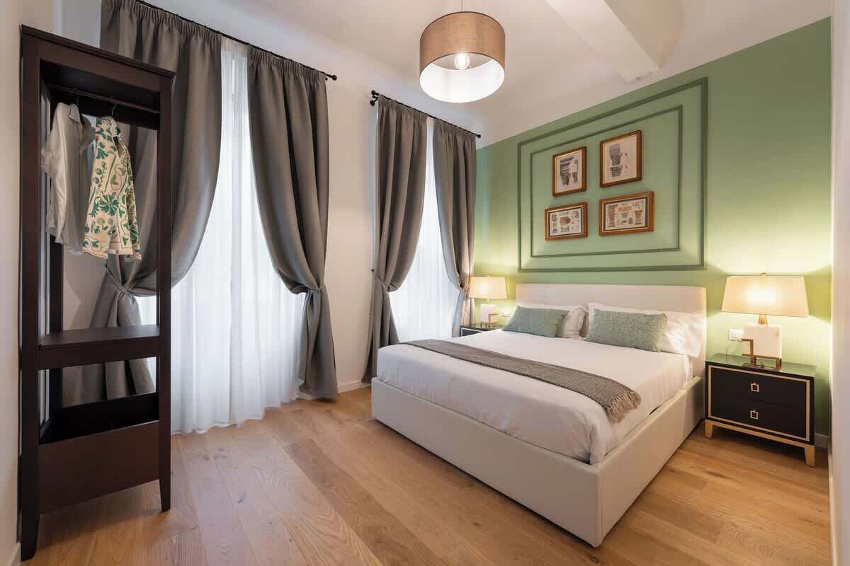 A bedroom with a bed, a wardrobe, a nightstand, and a wall with framed pictures.