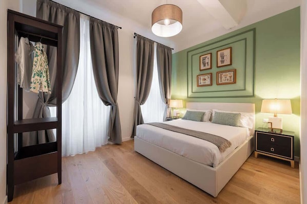 A bedroom with a bed, a wardrobe, a nightstand, and a wall with framed pictures.