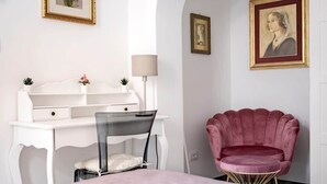 Une pièce avec un bureau blanc, une chaise et un fauteuil rose, ainsi qu’un lit.
