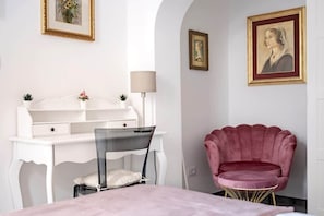 A room with a white desk, a chair, a pink chair, and a bed.