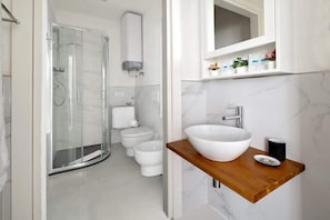 A modern bathroom with a glass shower enclosure, a white sink with a wooden countertop, and a toilet.