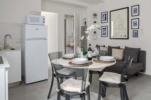 Une cuisine moderne dotée d’un réfrigérateur encastré, d’une table à manger pour quatre personnes et d’un canapé gris dans l’espace salon.