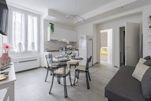 A modern kitchen with white cabinets, a dining table set for four, and a refrigerator.