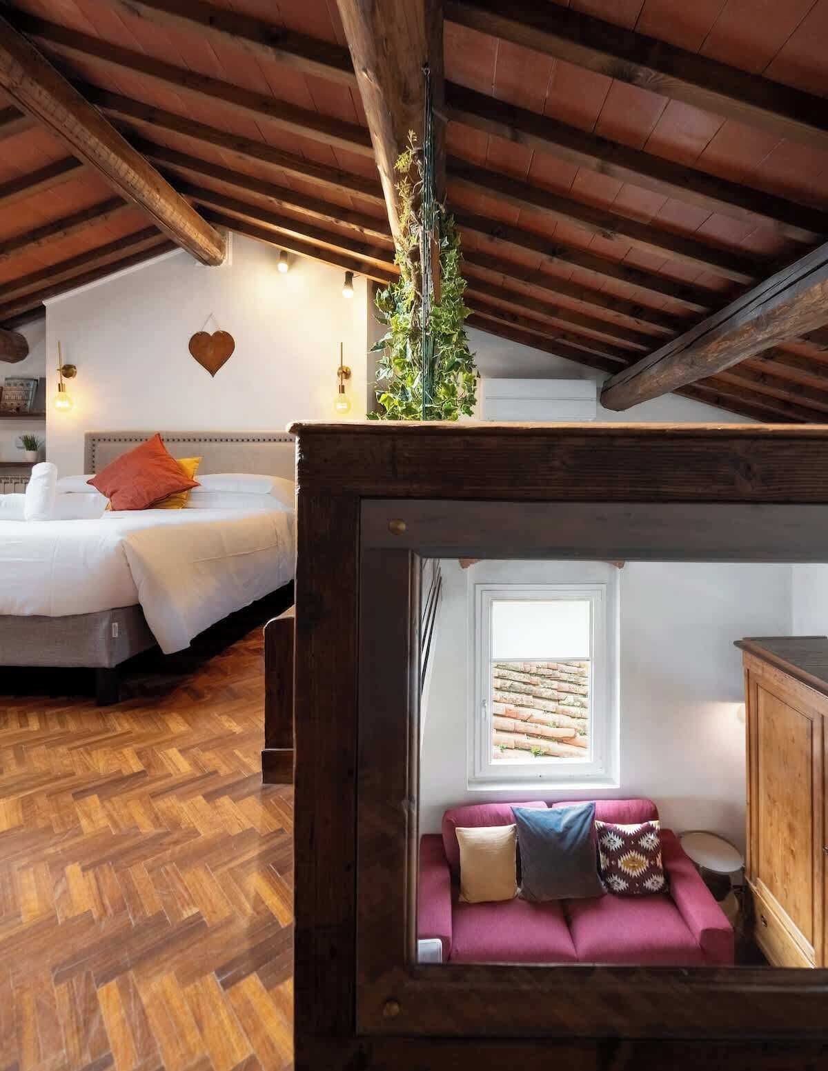 A cozy room with a bed, a small sofa, a heart-shaped wall decoration, and a hanging plant.