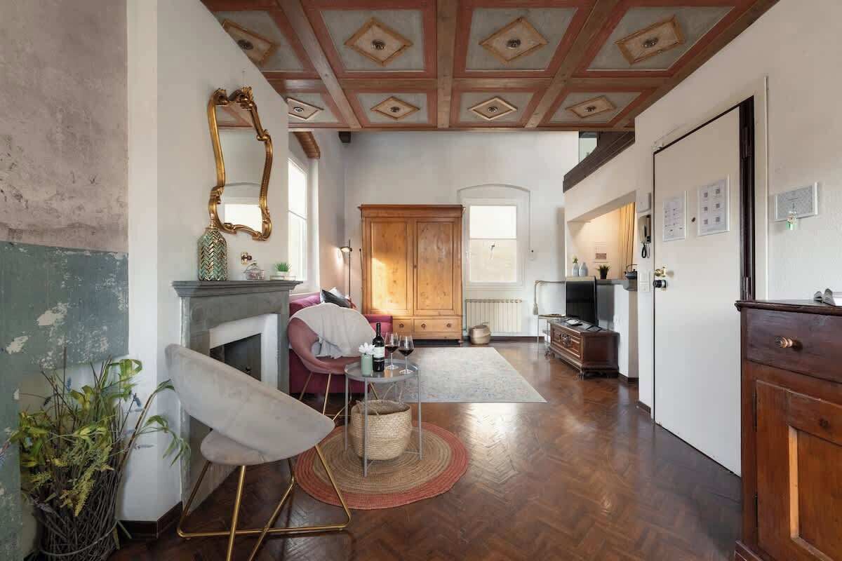 A room with a wooden ceiling, a fireplace, a dining area, and a kitchen.