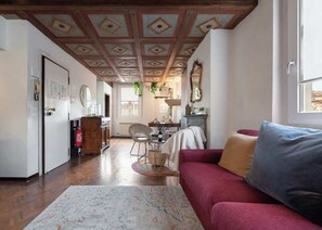 Una sala de estar con un sofá rojo, un tapete estampado y techo de madera.