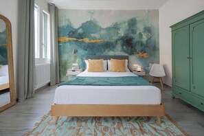 A bedroom with a bed, a green wardrobe, a large abstract painting on the wall, and a window with curtains.