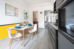 A modern kitchen with a dining area, featuring a black countertop, white chairs, and a yellow accent wall.